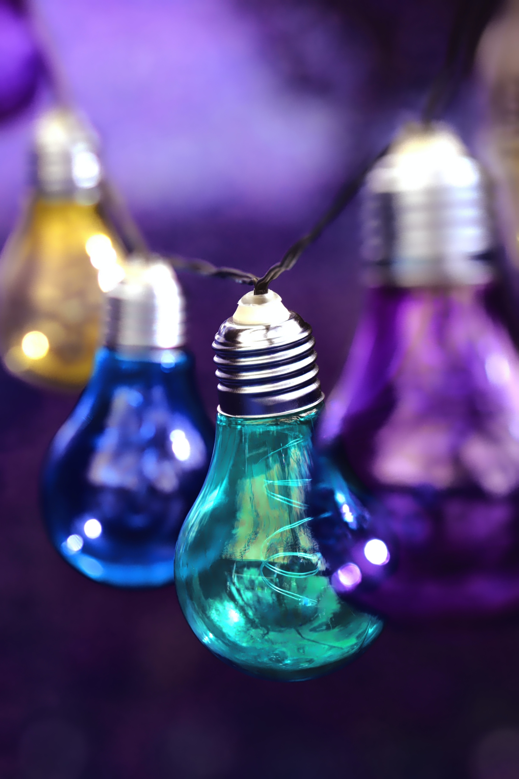 Coloured, hanging light bulbs with purple background